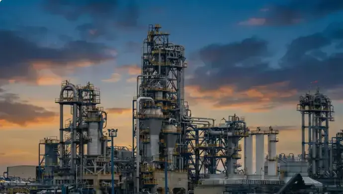 A large industrial oil refinery complex at sunset with a cloudy sky.