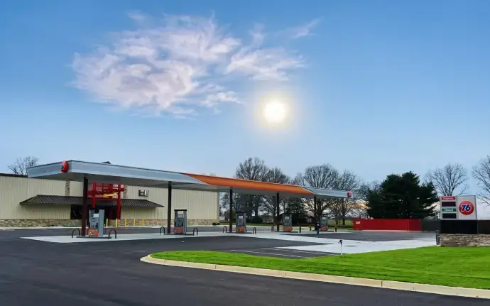 A modern '76' gas station under a bright sun and blue sky.